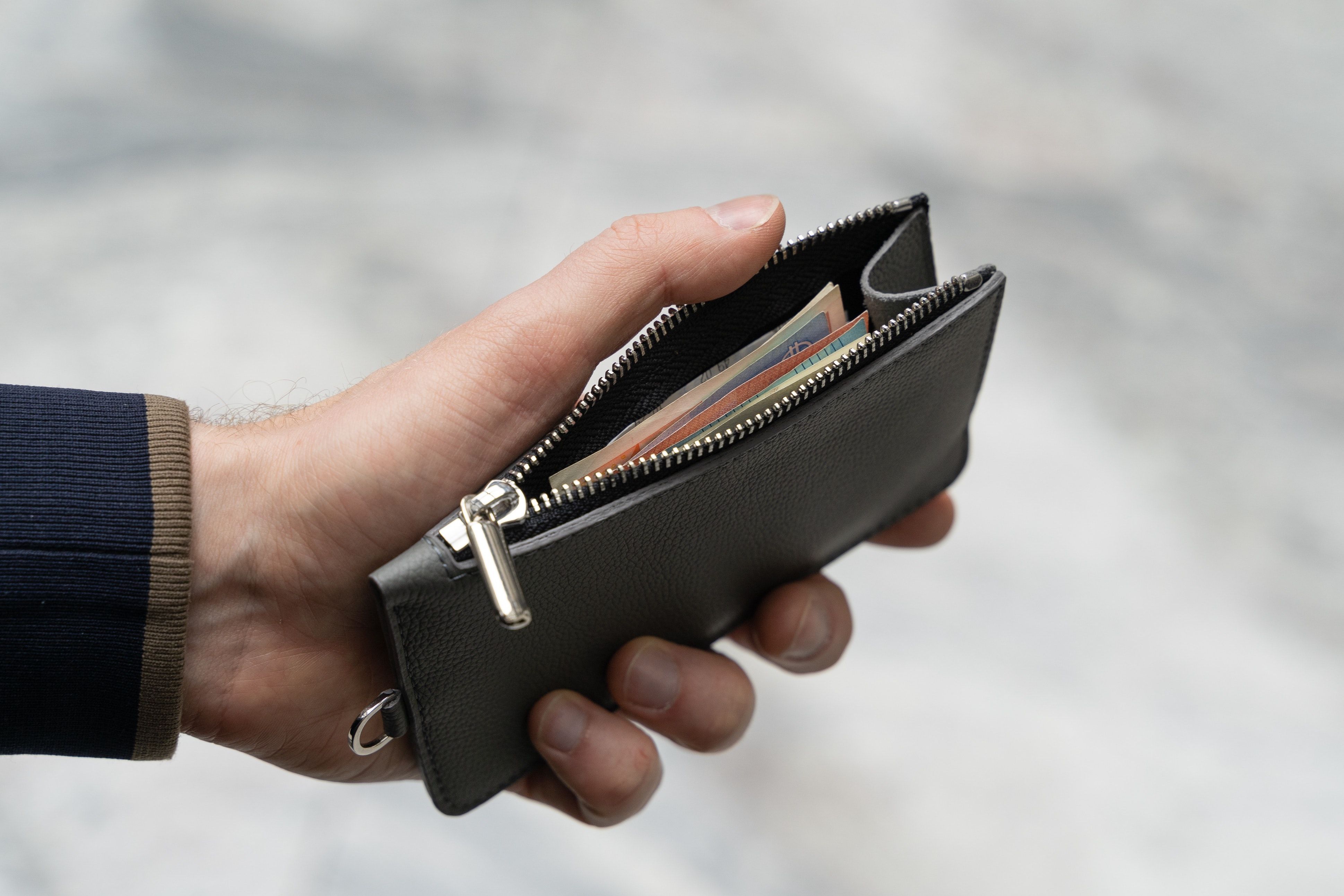 Hand holding an open wallet, against a soft-focus gray background