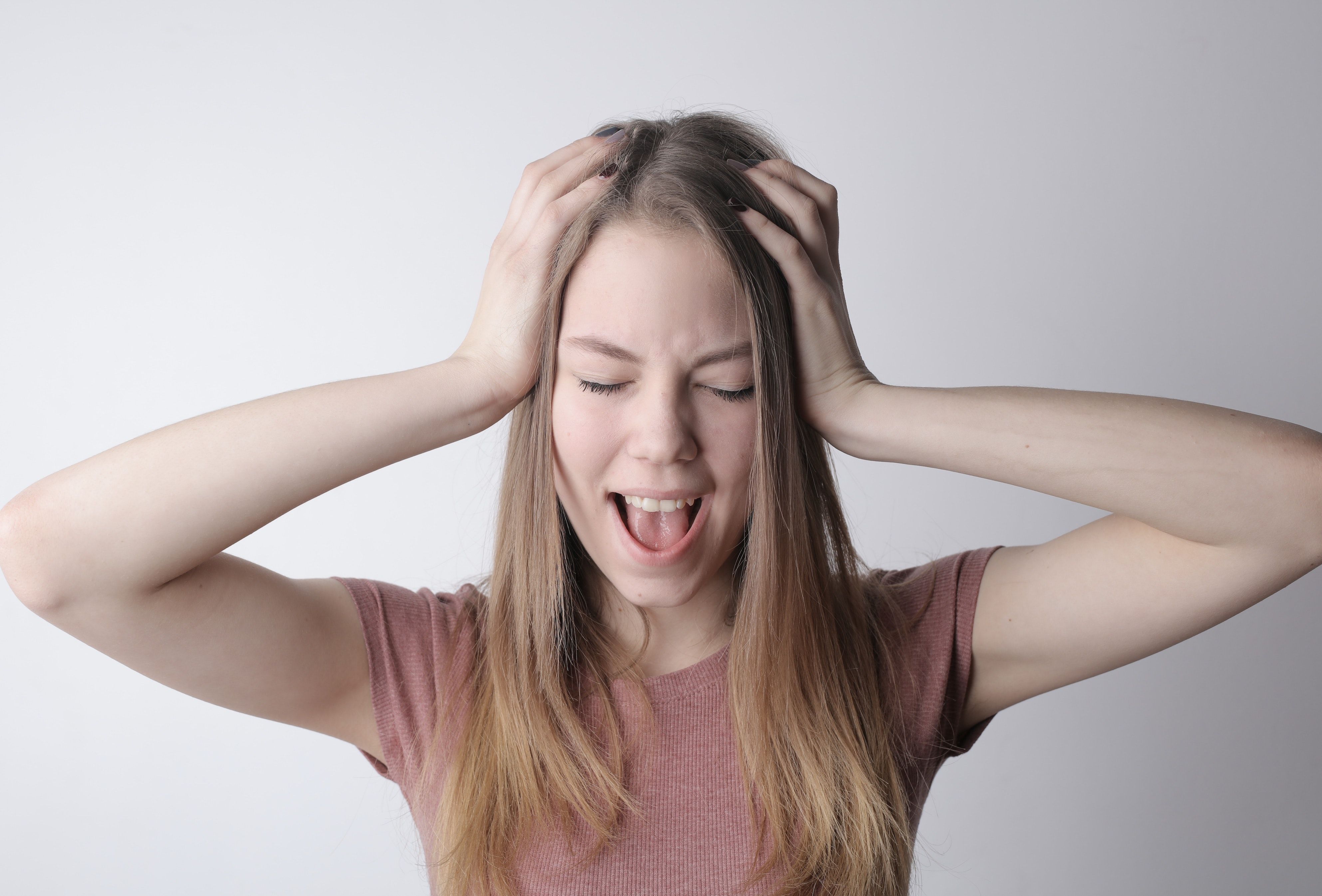 Open-mouthed girl in mauve shirt raises her hands to her head in frustration