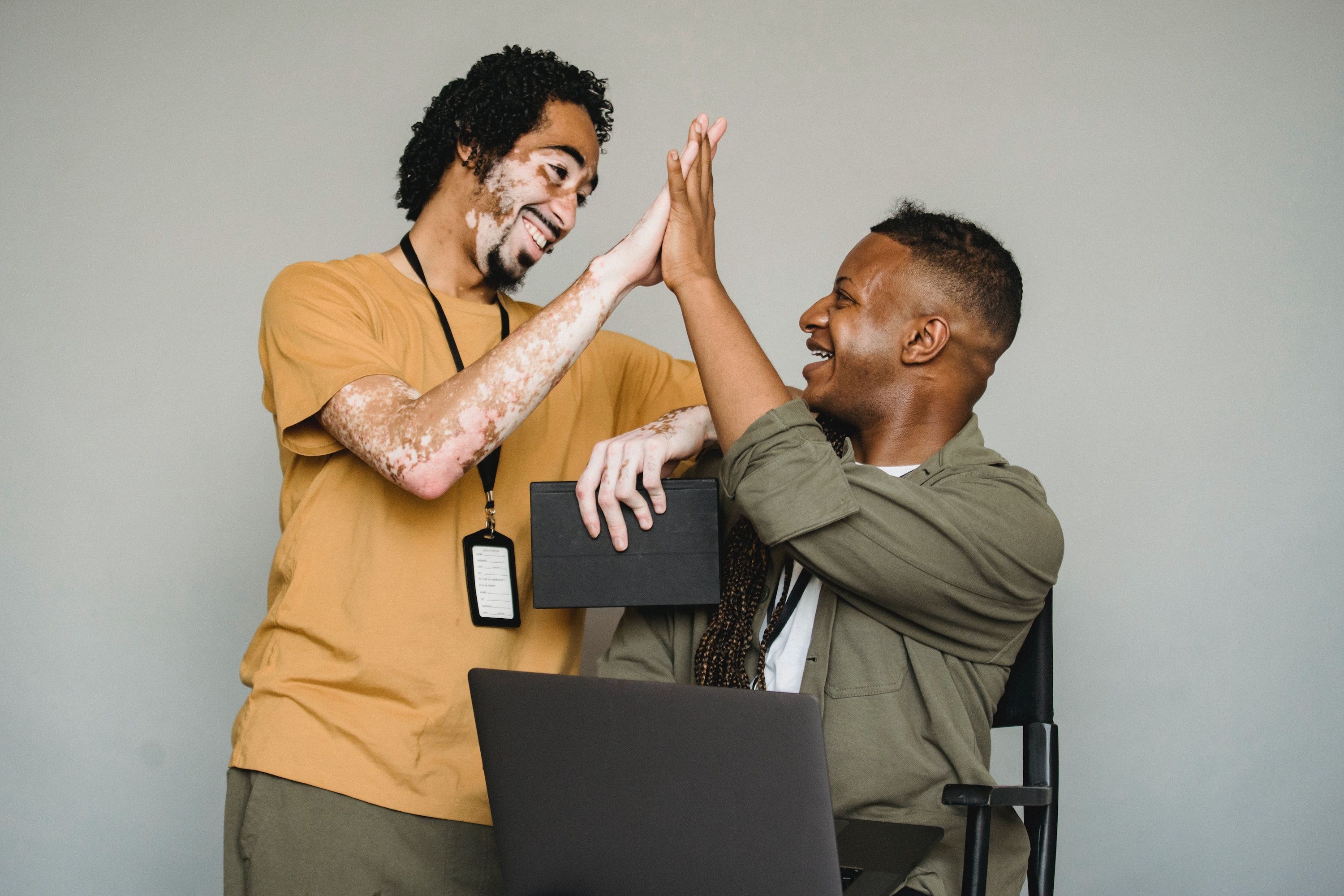 Two men smile and high-five each other, an open laptop in front of them