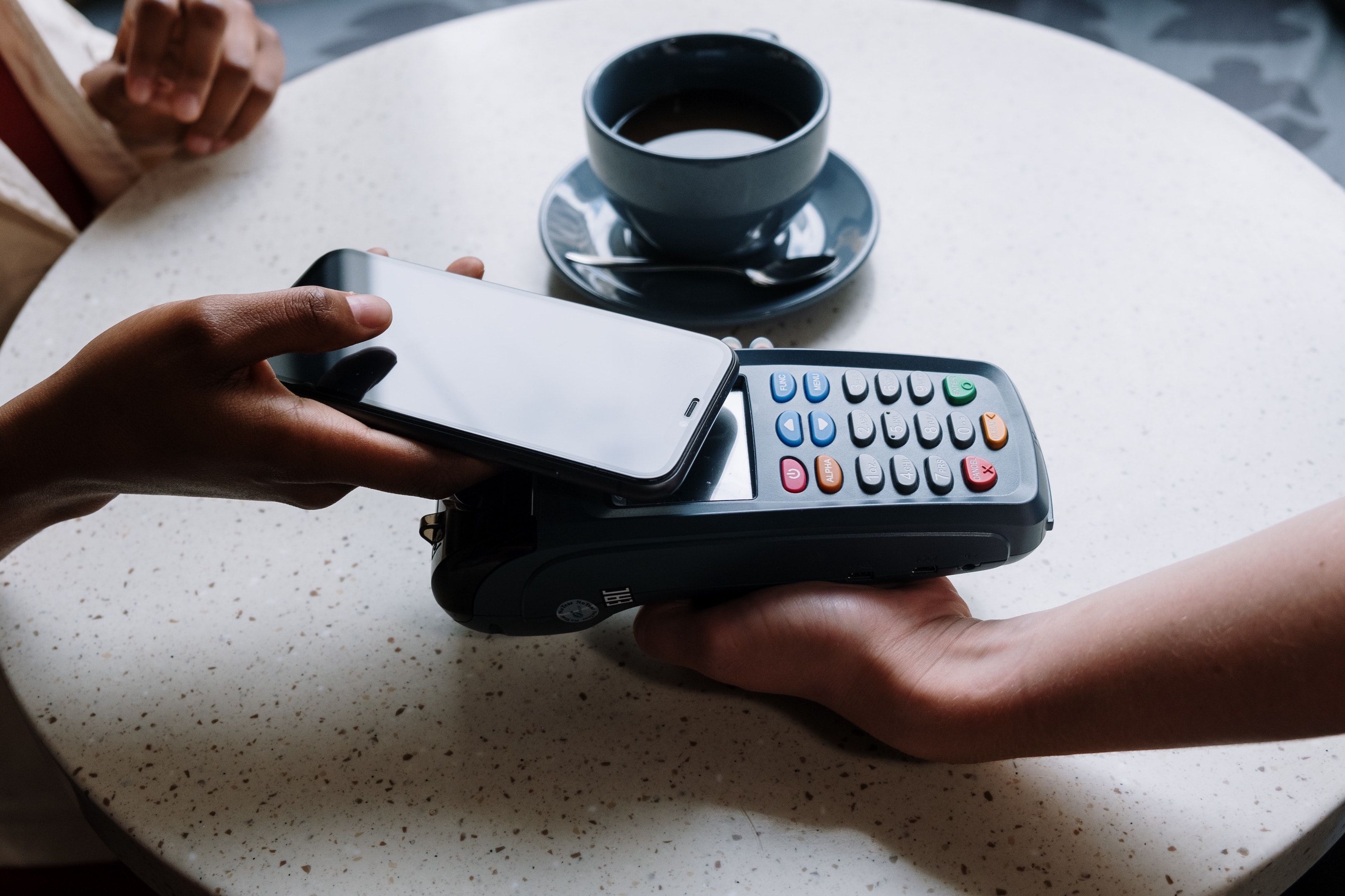 Atop a coffee table, a person taps a cardreader with an iPhone to make a purchase