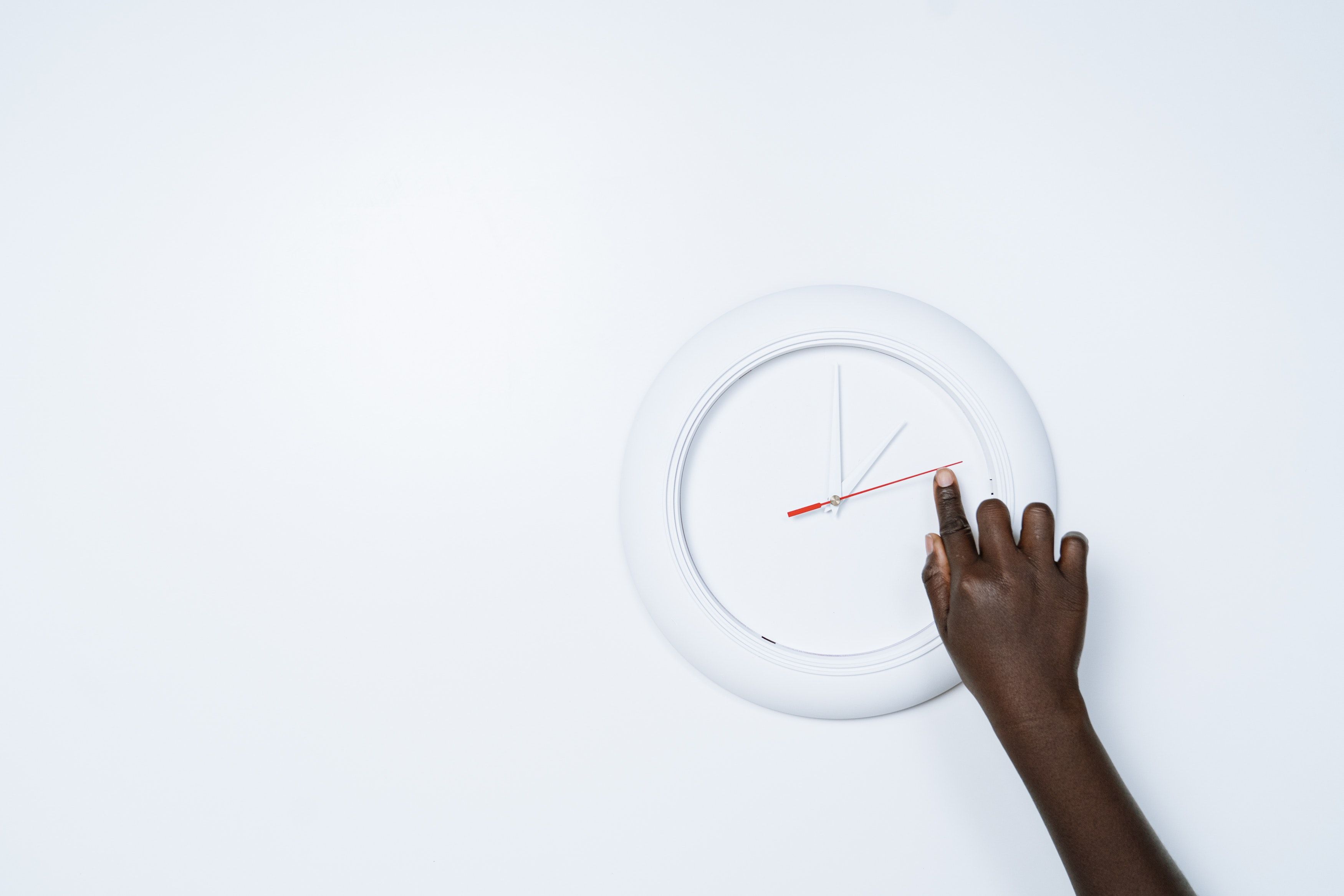 Hand reaches up to touch white clock face, mounted on a white wall