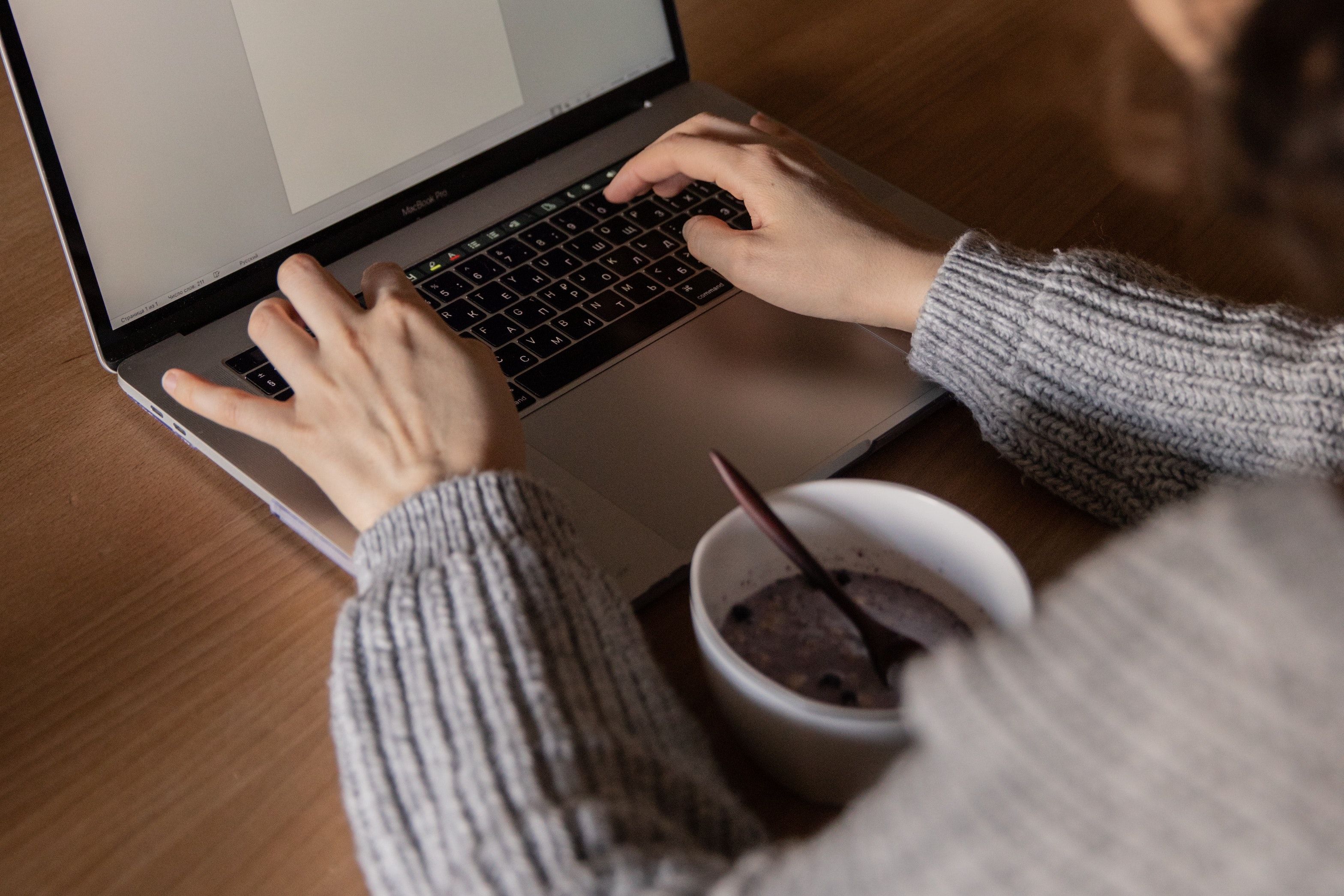 Person in gray sweater types on laptop with a mug