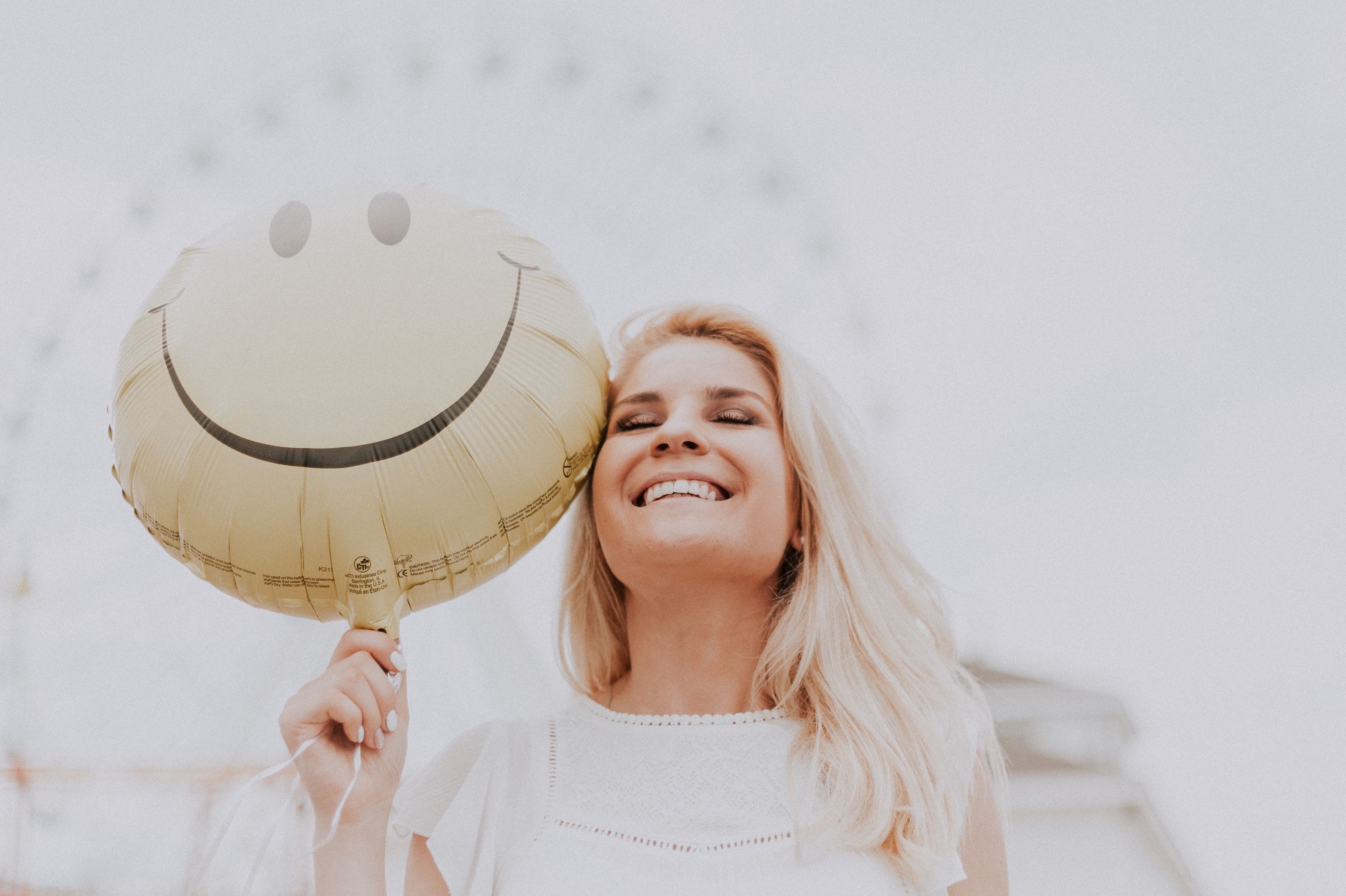 Blonde girl smiles in front of ferris wheel, holding smiley-face helium balloon