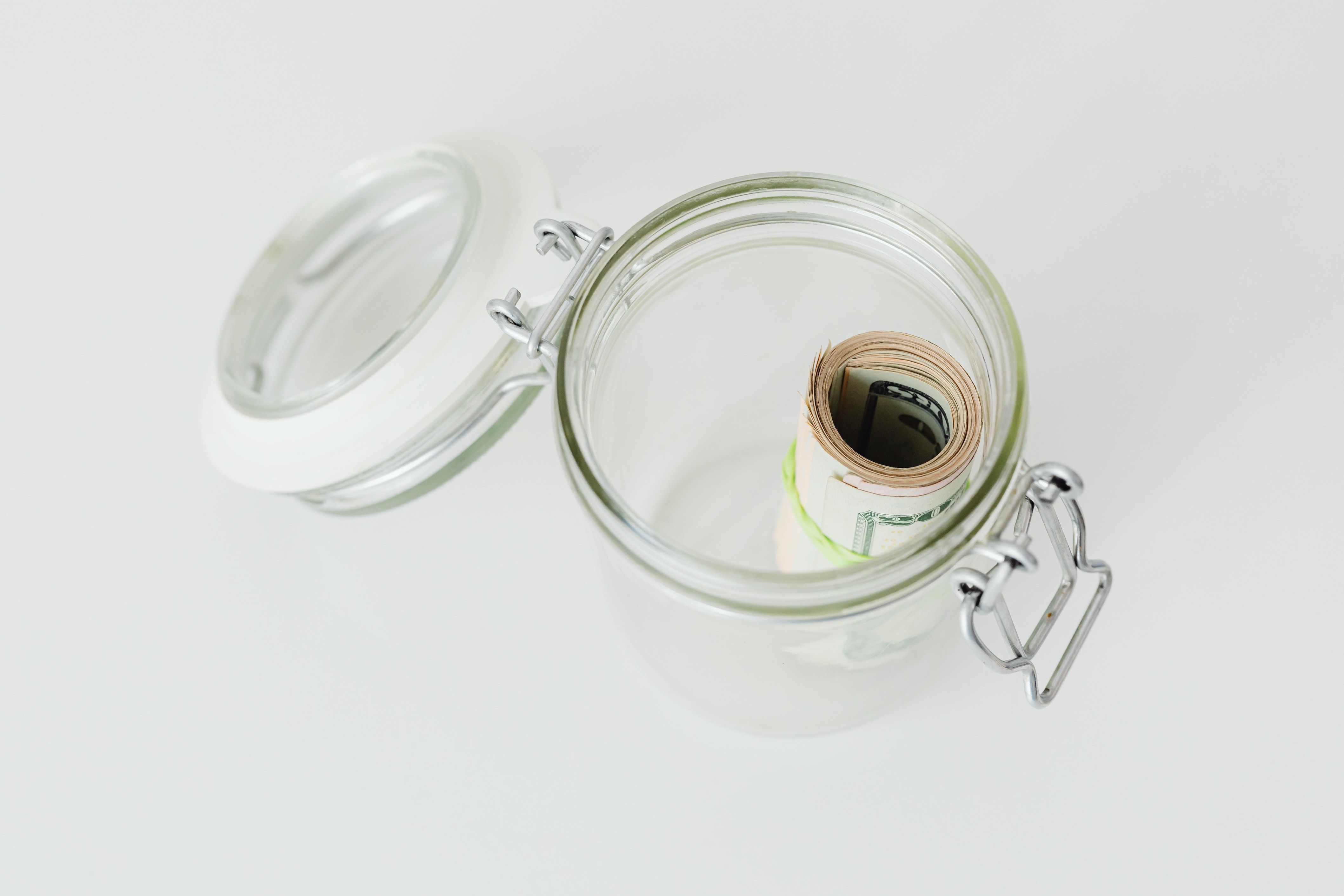 Roll of bills in open glass jar, on a white surface