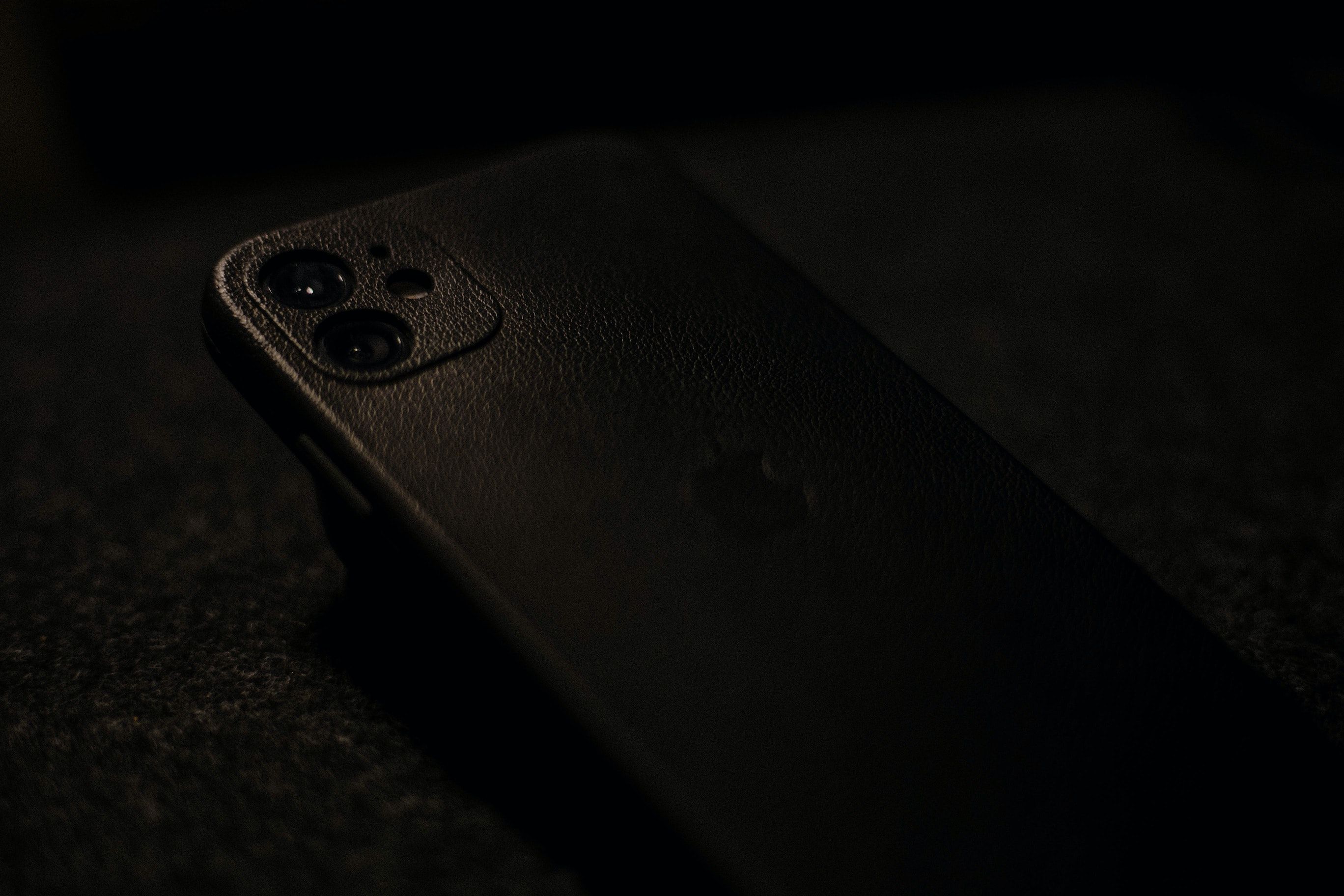 Barely visible black iPhone in black leather case, against a black background