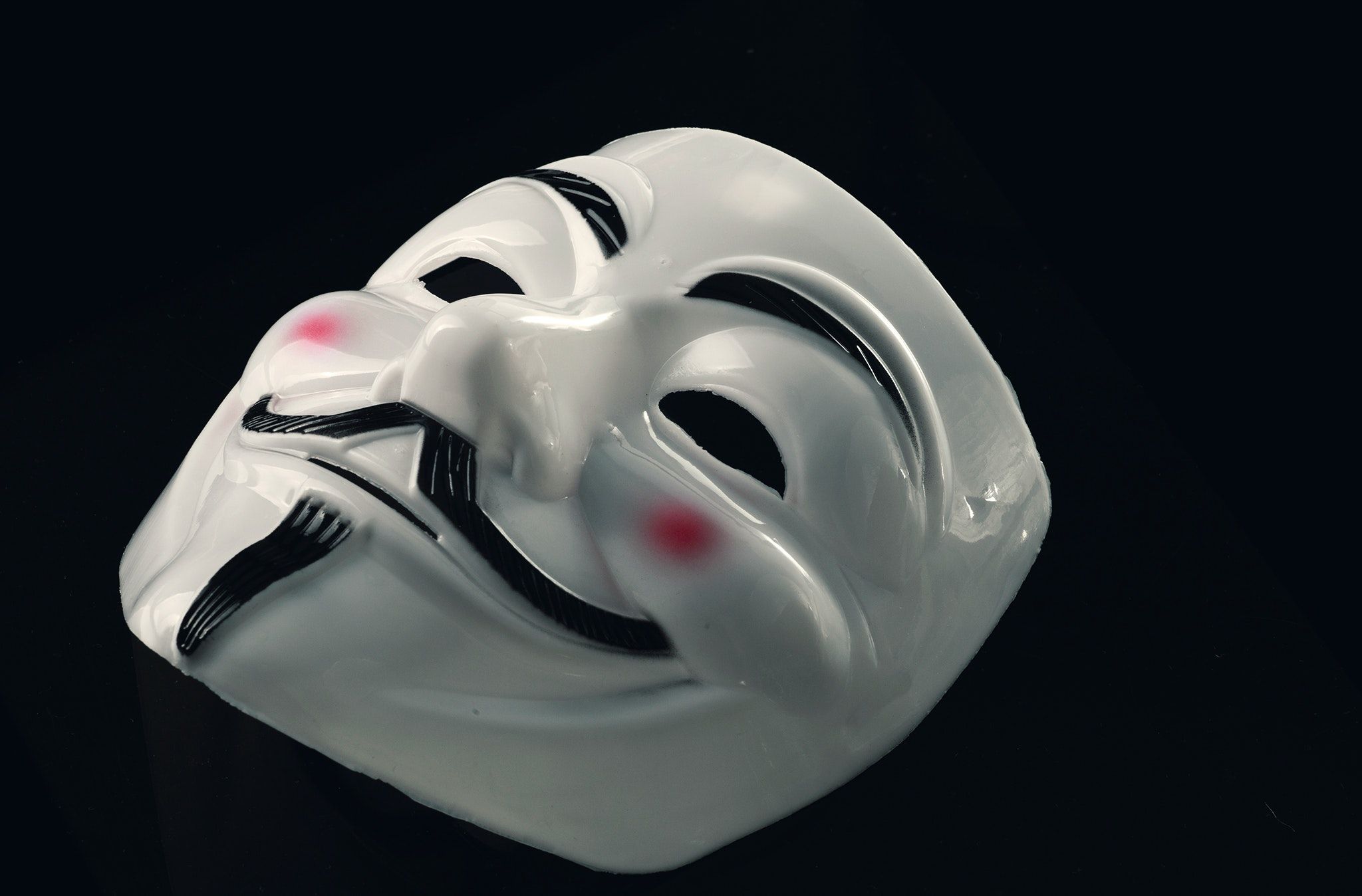 Theatrical mask associated with hackers lies flat on a black surface