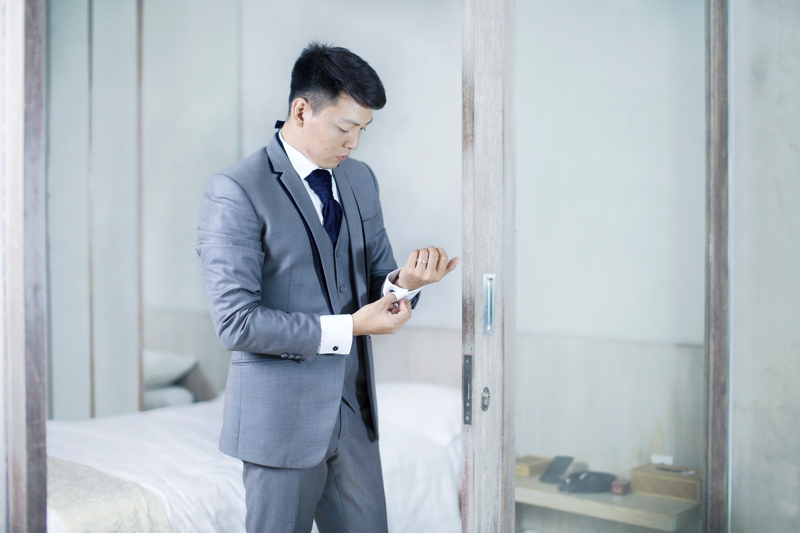 Man in gray suit adjusts his sleeves inside a glass-walled office