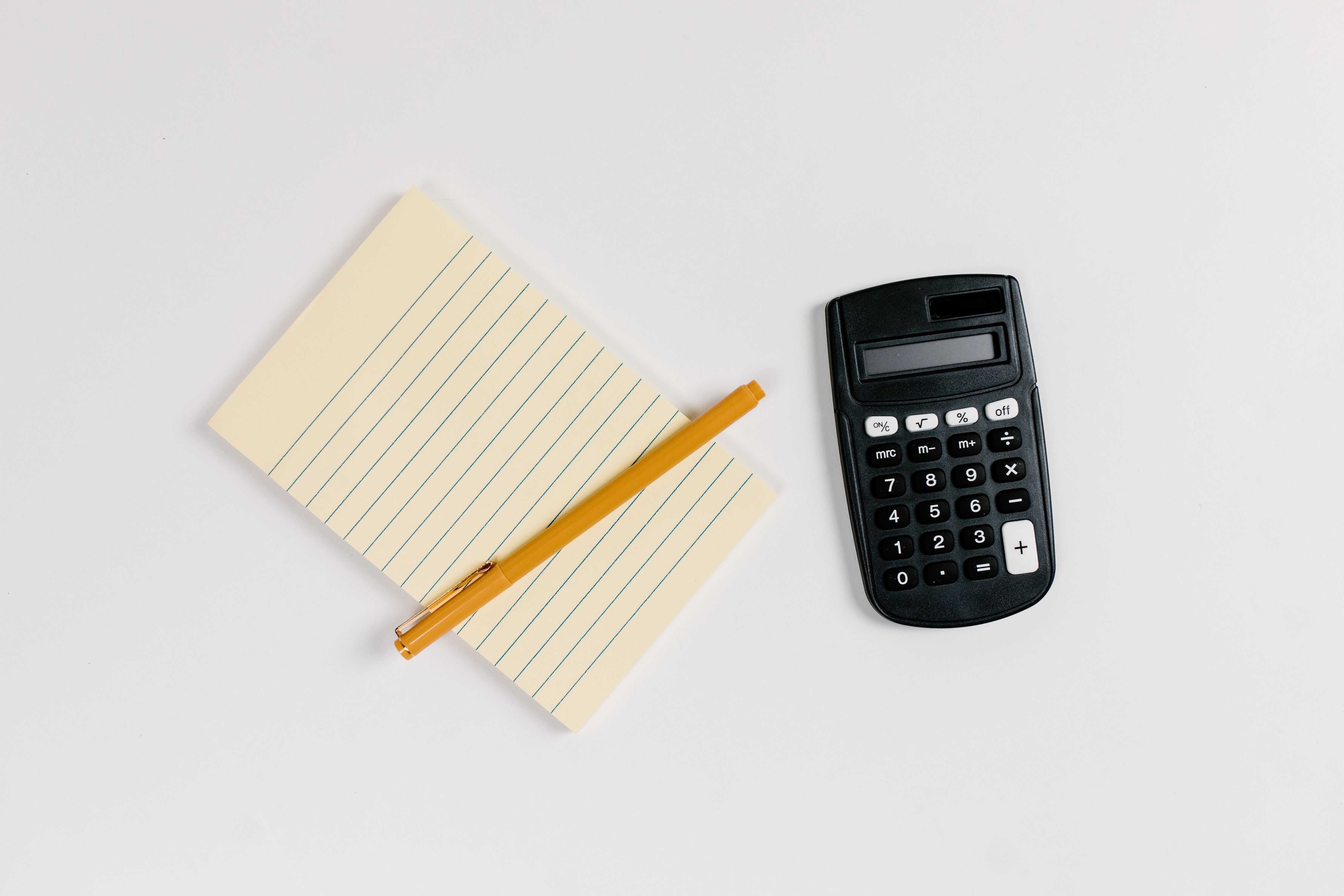 Flat lay of black calculator and notepad with pen, on a white surface