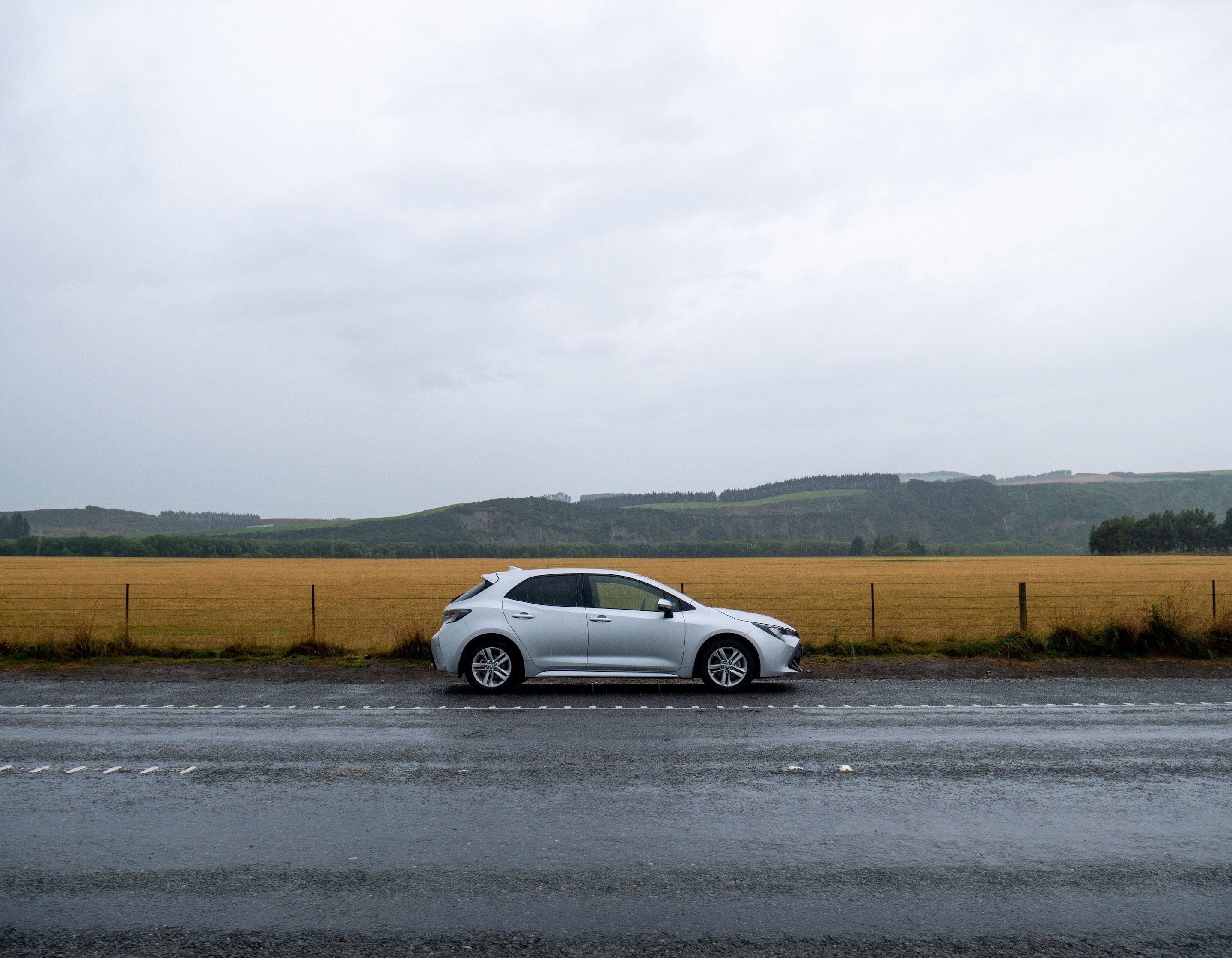 Lone silver hatchback on a country road, with hills in the background