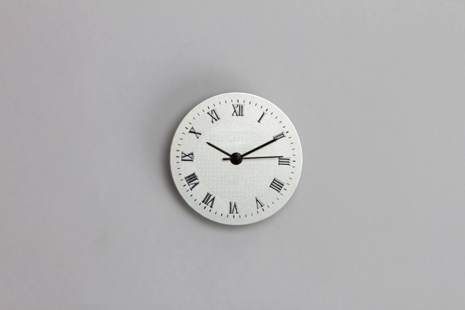 White wall clock with roman numerals displays 10:10, on a gray wall